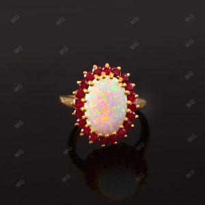Puede incluir: Un anillo de oro con una gran opala ovalada rodeada por un halo de rubíes rojos.
