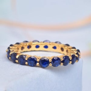 Puede incluir: Un anillo de banda de oro con una fila de zafiros azules redondos.
