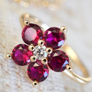 Puede incluir: Un anillo de oro con un diseño de flor con cinco piedras de rubí y un solo diamante en el centro.