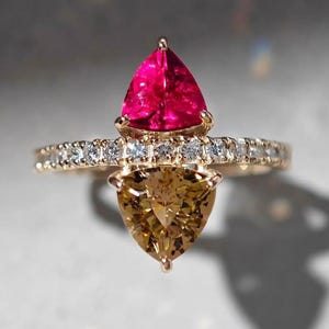 Puede incluir: Un anillo de oro con una piedra preciosa roja y marrón engastada en el centro. El anillo está rodeado por una banda de pequeños diamantes.