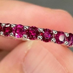 Puede incluir: Un anillo de banda de plata con una fila de piedras redondas de rubí rojo oscuro.