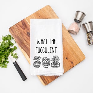 May include: White kitchen towel with the text "What the Fucculent" and a black and white illustration of four potted succulents.