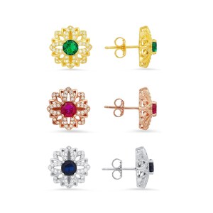 May include: Set of three pairs of flower-shaped earrings with a single gemstone in the center. The earrings are available in gold, rose gold, and silver with green, red, and blue gemstones.