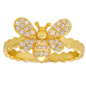 May include: A gold ring with a bee design. The bee is covered in clear sparkling stones. The band of the ring is textured.