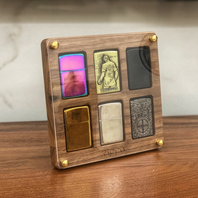May include: A wooden display case with a clear acrylic front, showcasing six different Zippo lighters. The lighters are arranged in a grid pattern, with each lighter having a unique design. The case is made of dark wood with brass accents and the word "Zippo" is engraved on the bottom.