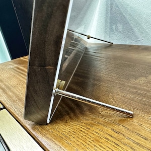 May include: A wooden frame with a clear acrylic front and a metal stand. The stand is adjustable and can be used to prop up the frame.