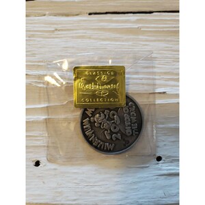 Puede incluir: Un paquete de plástico transparente que contiene una etiqueta rectangular dorada y una moneda plateada. La etiqueta dice "Classics Collection Walt Disney" en letras doradas. La moneda presenta a Mickey Mouse y el texto "2000 Millennium On Top of the World."