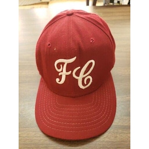 May include: A red baseball cap with a white "FC" logo embroidered on the front. The cap has a curved brim and a structured crown.