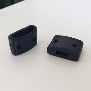 May include: Two black plastic buckles with two holes each. The buckles are designed to be used for straps or belts.
