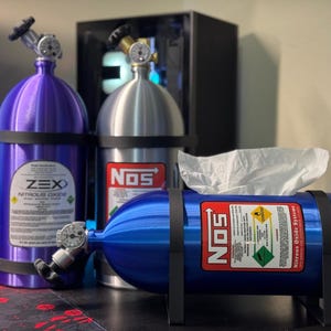 Puede incluir: Colección de artículos novedosos diseñados para parecerse a tanques de óxido nitroso. Los artículos incluyen un tanque ZEX morado, un tanque NOS plateado y un porta-pañuelos NOS azul. Cada artículo tiene un medidor y bandas negras.