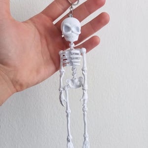 May include: A white plastic skeleton keychain with a skull head and articulated limbs.