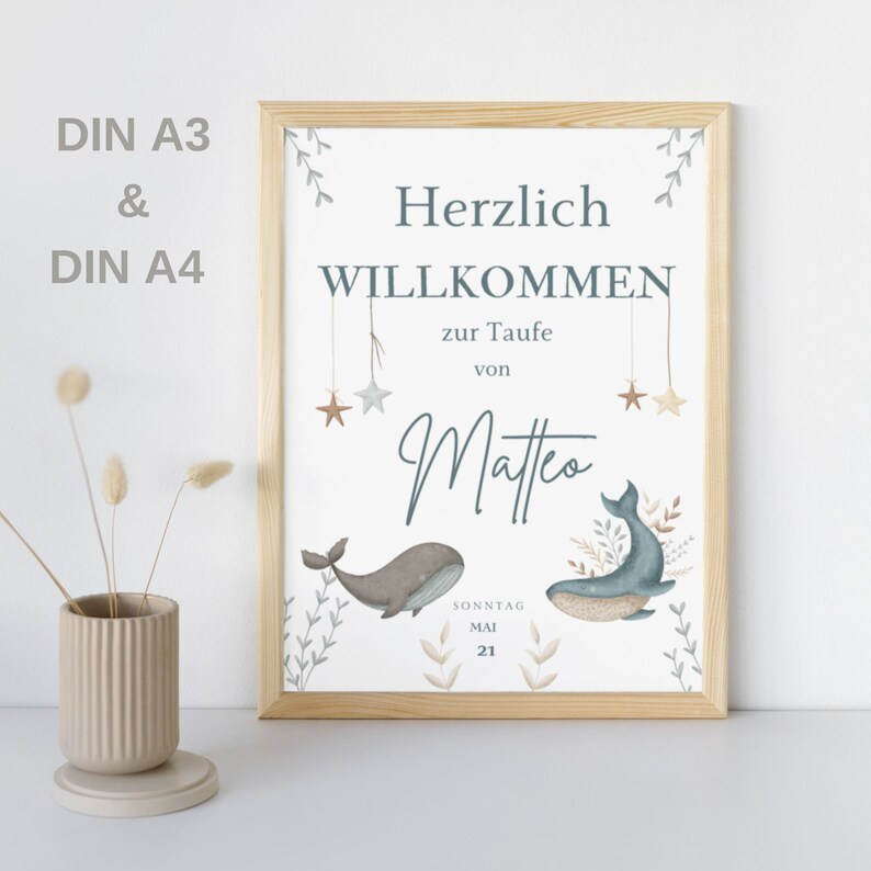 Puede incluir: Una impresi&oacute;n enmarcada blanca con un dise&ntilde;o de ballena azul y marr&oacute;n. El texto dice "Herzlich Willkommen zur Taufe von Matteo Sonntag Mai 21".