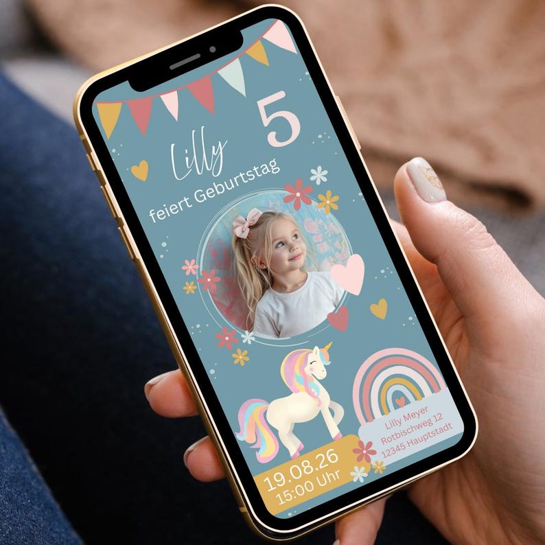 Ein Smartphone zeigt eine Geburtstagseinladung mit einem Foto eines kleinen Mädchens. Das Design der Einladung zeigt ein Einhorn, einen Regenbogen, Blumen.