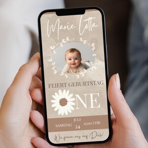 Puede incluir: Un tel&eacute;fono inteligente muestra una invitaci&oacute;n digital para el primer cumplea&ntilde;os de un beb&eacute;. La invitaci&oacute;n presenta una foto del beb&eacute;, adornos florales y texto en alem&aacute;n, incluido el nombre "Marie Lotta" y la fecha.