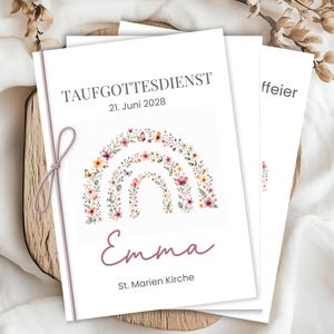 May include: White event program with the text "TAUF GOTTESDIENST 21. Juni 2028" and the name "Emma". A floral rainbow design with butterflies and flowers decorates the front. A pink ribbon is tied to the side.