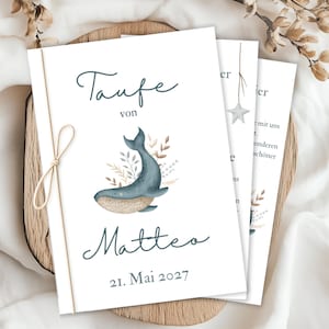 Op de afbeelding: Witte uitnodigingskaarten met een aquarel walvis illustratie en de tekst "Taufe von Matteo 21. Mai 2027". De kaarten zijn vastgebonden met een beige touwtje en liggen op een houten dienblad.