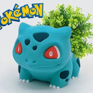 Puede incluir: Un macetero Pokemon azul y verde con forma de Bulbasaur, un Pokemon de tipo planta. El macetero tiene una pequeña abertura en la parte superior para plantar. El macetero está hecho de plástico y tiene un acabado liso.