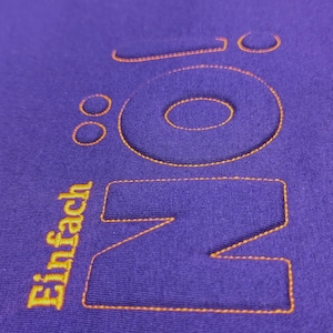 Puede incluir: Sudadera morada con la palabra "NO" en letras grandes bordadas en naranja. La palabra "Einfach" est&aacute; bordada en naranja debajo de la "NO".