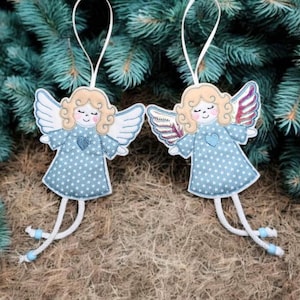 Op de afbeelding: Twee engelenornamenten met lichtblauwe jurken versierd met witte sterren en witte vleugels. De engelen hebben blond krullend haar en een hart op hun borst. Elk ornament heeft een wit touwtje om op te hangen.