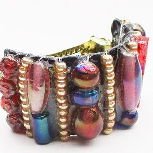 May include: A black leather hair clip with a gold clasp and a row of iridescent beads in shades of red, pink, blue, and gold.