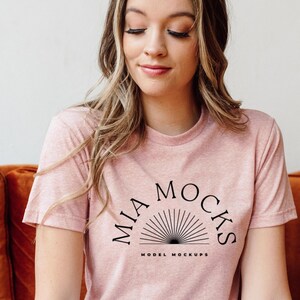 Op de afbeelding: Een roze T-shirt met een zwart grafisch ontwerp met de tekst "MIA MOCKS MODEL MOCKUPS" en een gestileerde zon.