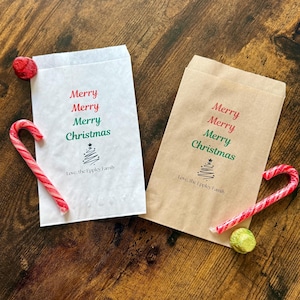 May include: Two Christmas-themed gift bags, one white and one brown, with the words "Merry Christmas" printed in red and green. Each bag has a candy cane and a piece of candy next to it. The bags also have the text "Love, the Eppley Family".