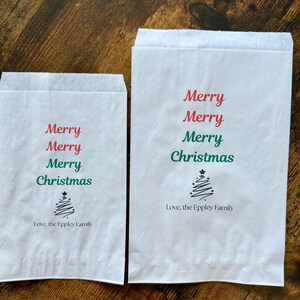 May include: Two white paper gift bags with the words "Merry Christmas" in red and green. A stylized Christmas tree is below the text, and the phrase "Love, the Eppley Family" is printed at the bottom.