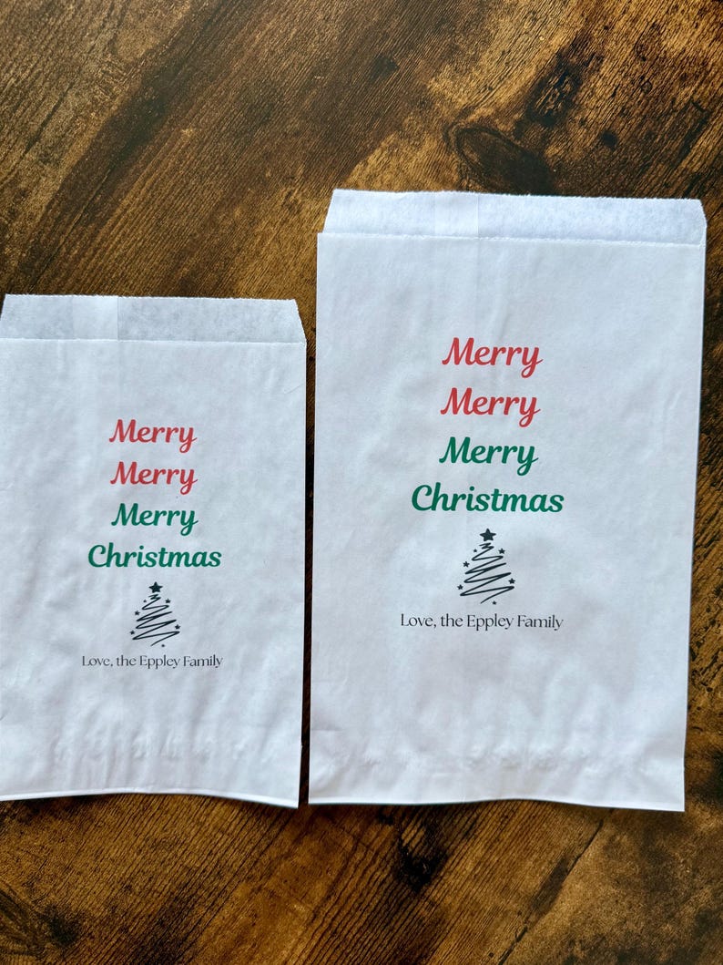 May include: Two white paper gift bags with the words "Merry Christmas" in red and green. A stylized Christmas tree is below the text, and the phrase "Love, the Eppley Family" is printed at the bottom.