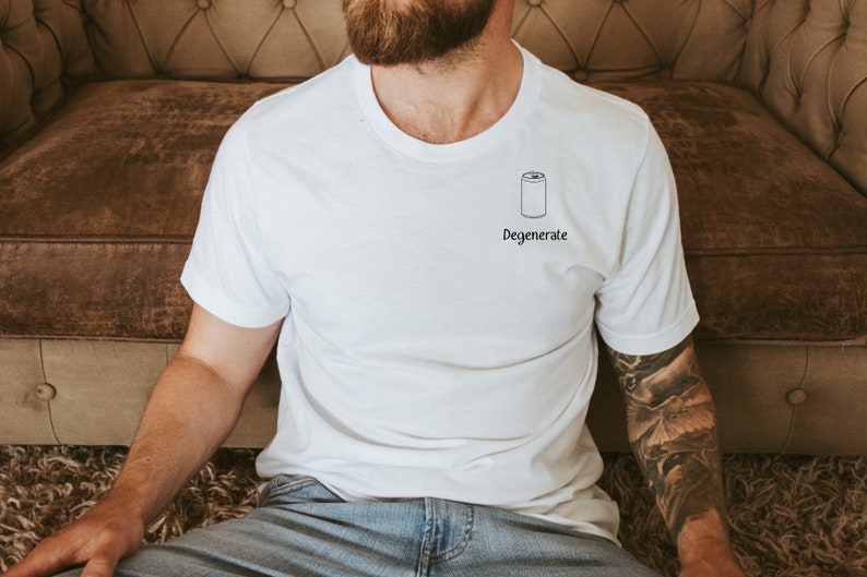 Op de afbeelding: Wit T-shirt met een zwarte illustratie van een blikje en het woord "Degenerate" eronder. Het shirt heeft korte mouwen en een ronde hals.