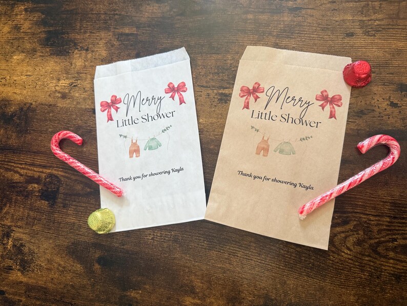 May include: Two paper gift bags with the text "Merry Little Shower" and baby clothes illustrations. Red bows and candy canes decorate the scene. One bag is white, the other is brown. A gold foil-wrapped chocolate coin is also present.