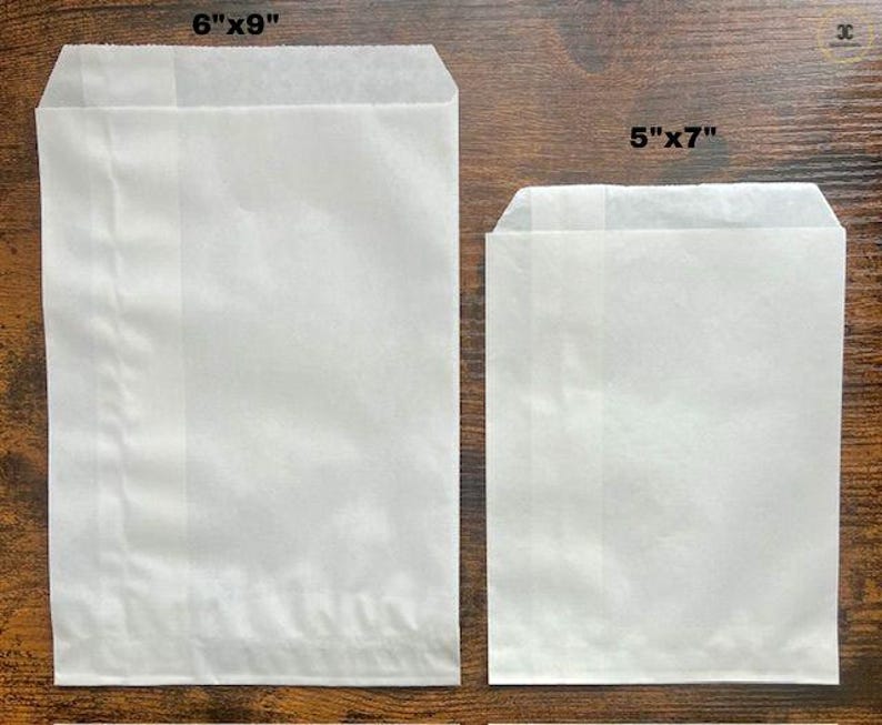 May include: Two rectangular white paper bags with a semi-translucent finish. The larger bag is labeled 6"x9" and the smaller bag is labeled 5"x7". Both bags feature a flat bottom construction and a simple open top design for storage.