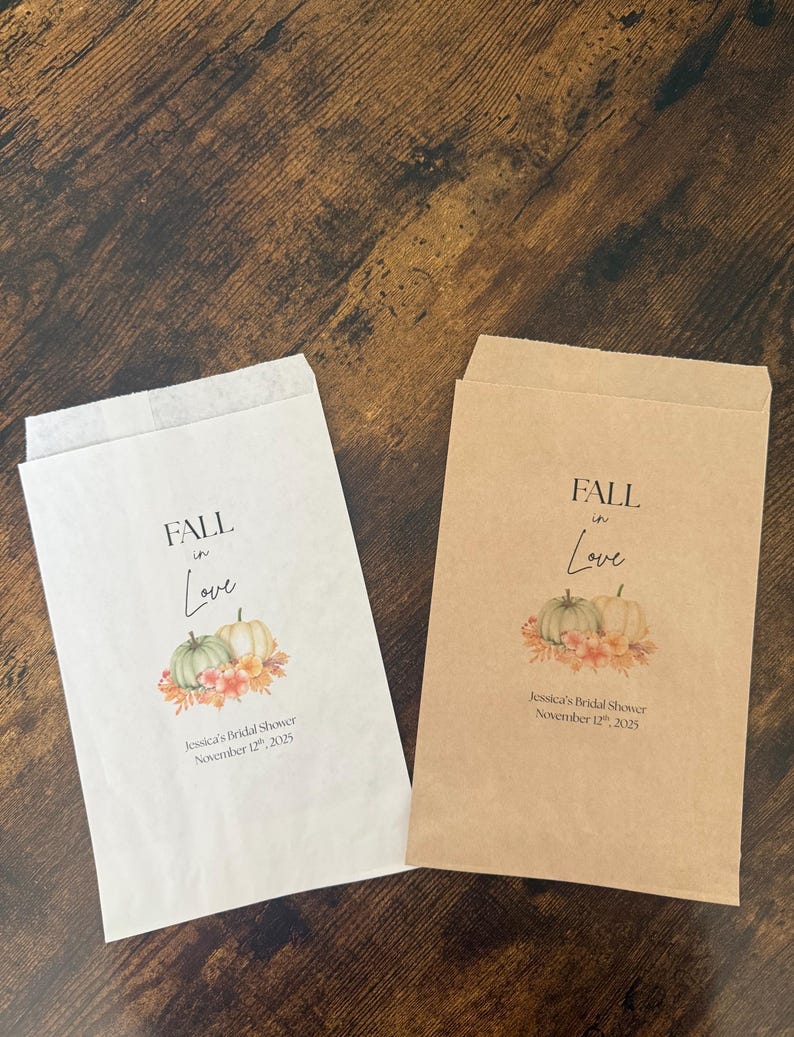 May include: Two paper favor bags, one white and one brown, with a fall-themed design. The bags feature the text "FALL in Love" above a watercolor image of pumpkins and flowers. The text "Jessica's Bridal Shower November 12th, 2025" is also printed.