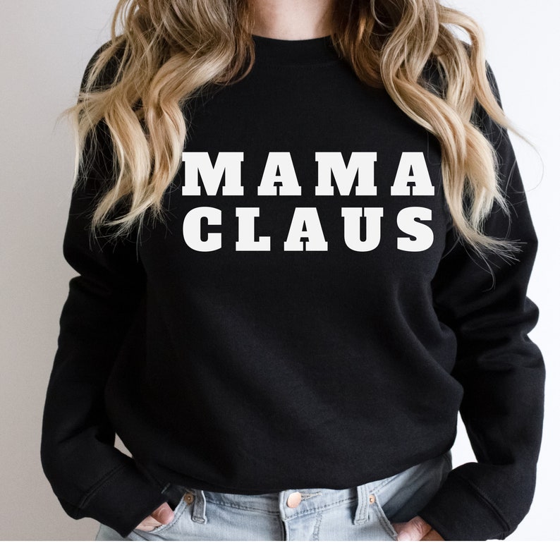 Op de afbeelding: Zwarte sweatshirt met de witte tekst "MAMA CLAUS" in vette letters. De tekst is gecentreerd op de borst. De sweatshirt heeft een ronde hals en lijkt van zacht materiaal te zijn.