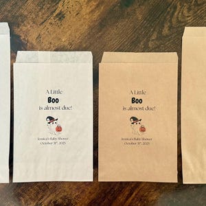 K&ouml;nnte beinhalten: Vier Papiert&uuml;ten, zwei wei&szlig;e und zwei braune, mit dem Text "A Little Boo is almost due!" und einer Geisterillustration. Die T&uuml;ten sind f&uuml;r eine Babyparty, mit dem Datum unter der Illustration.