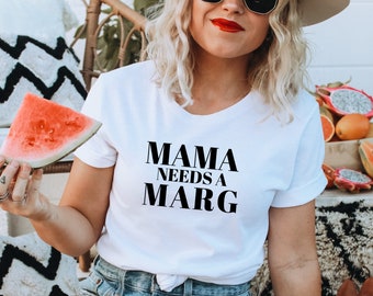 May include: White t-shirt with the text "MAMA NEEDS A MARG" in black block letters. The person is holding a slice of watermelon. The person is wearing sunglasses and a hat.