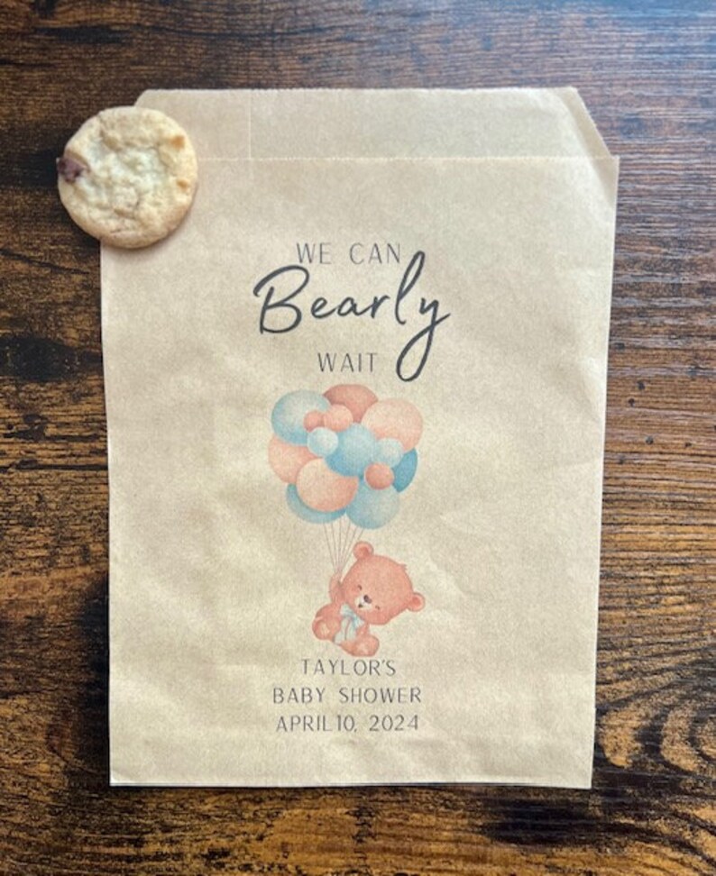 May include: A brown paper bag with a cookie and a baby shower design. The bag features a teddy bear holding balloons and the text "We Can Bearly Wait." The baby shower is for Taylor and is scheduled for April 10, 2024.
