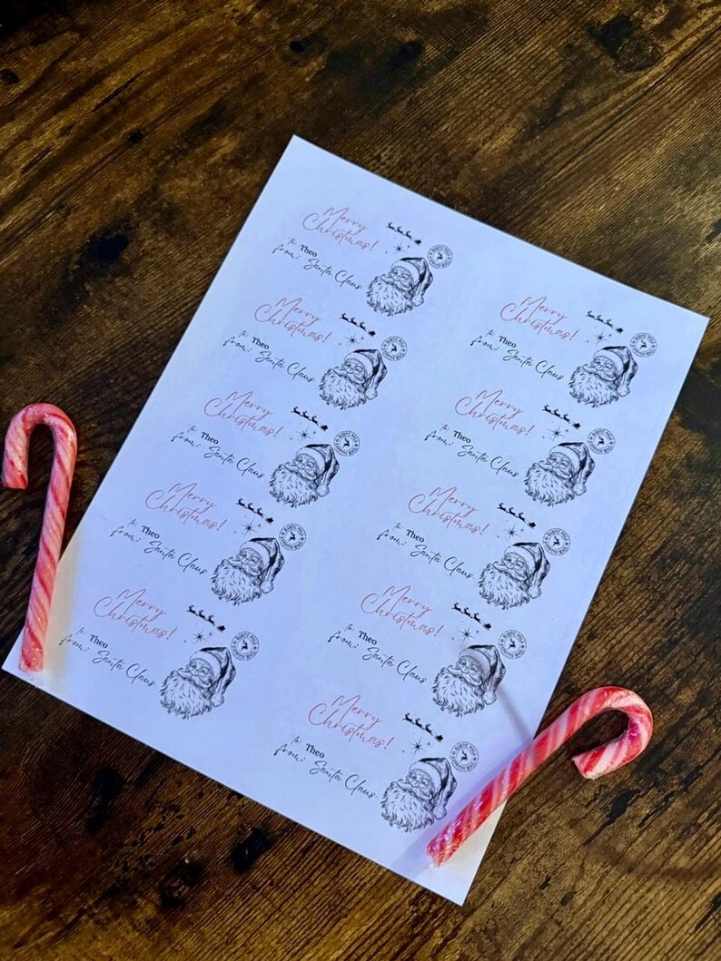 May include: A white sheet of paper featuring Santa Claus illustrations and the text "Merry Christmas!" and "Theo from Santa Claus." Two red and white candy canes rest on a wooden surface.