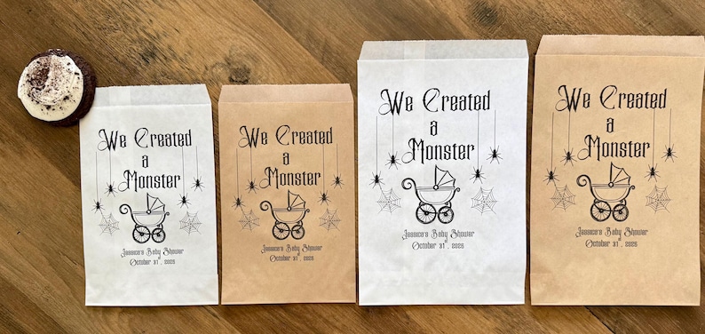 May include: Four rectangular paper favor bags in white and brown, featuring the black printed text We Created a Monster, a baby carriage icon, spider webs, and spiders, with the text Jameson's Baby Shower October 31, 2024 below the carriage.