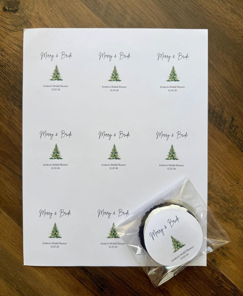 May include: A white sheet of paper featuring nine circular stickers with a watercolor green pine tree illustration, the text Merry & Bride, and the custom text Jessica's Bridal Shower 12.20.26. One sticker is placed inside a clear plastic bag.