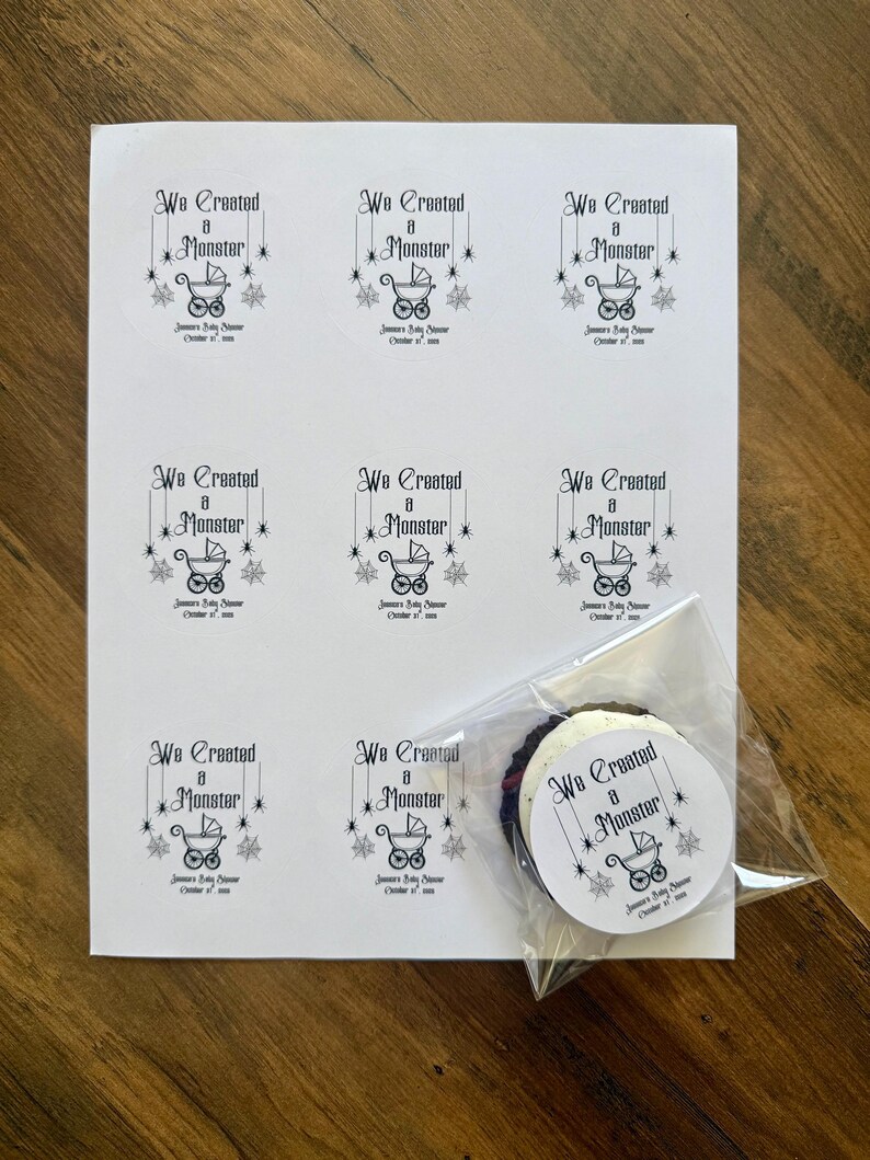 May include: A white sheet featuring eight printed rectangular labels and one circular label inside a clear plastic bag. Each label displays the black text We Created a Monster, a baby carriage icon, spider web accents, and the date October 31, 2023.