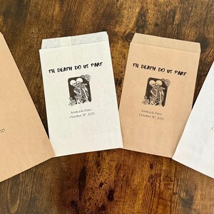May include: Four paper favor bags with the text "Til Death Do Us Part" and a skeleton couple graphic. The bags are in shades of brown and white, with the wedding date printed below the graphic.