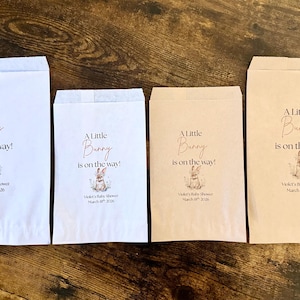 May include: Four paper treat bags in white and tan, with the text "A Little Bunny is on the way!" and a bunny illustration. The bags are for Violet's Baby Shower, March 18th, 2026.