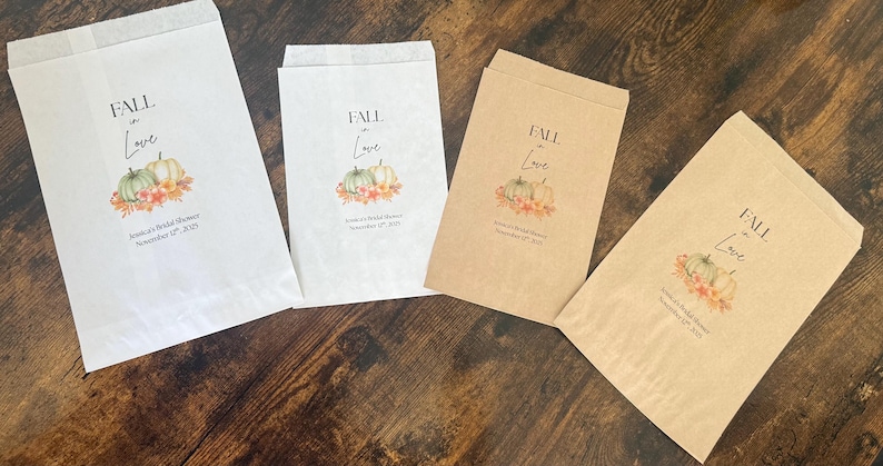 May include: Four paper favor bags with a fall theme. The bags are white and brown, with the words "FALL in Love" and a pumpkin design. Text below reads "Jessica's Bridal Shower November 17th, 2025."