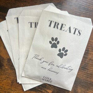 May include: White paper treat bags with the word "TREATS" in black, and two paw prints. The bags also have the text "Thank you for celebrating our humans" and the brand name "LOVE. MABLE."
