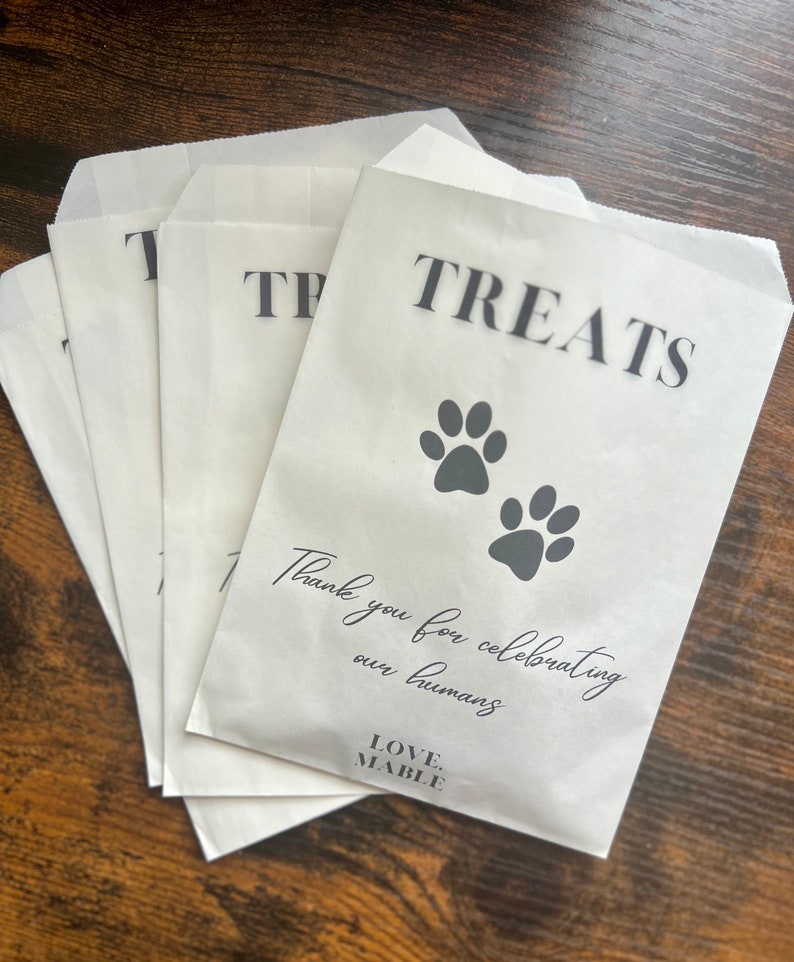 May include: White paper treat bags with the word "TREATS" in black, and two paw prints. The bags also have the text "Thank you for celebrating our humans" and the brand name "LOVE. MABLE."