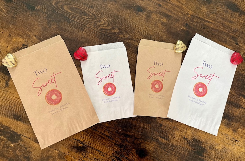 May include: Four paper treat bags with the words "Two Sweet" in red script, a donut graphic, and text. Two bags are brown, and two are white. Each bag is decorated with a heart-shaped candy.