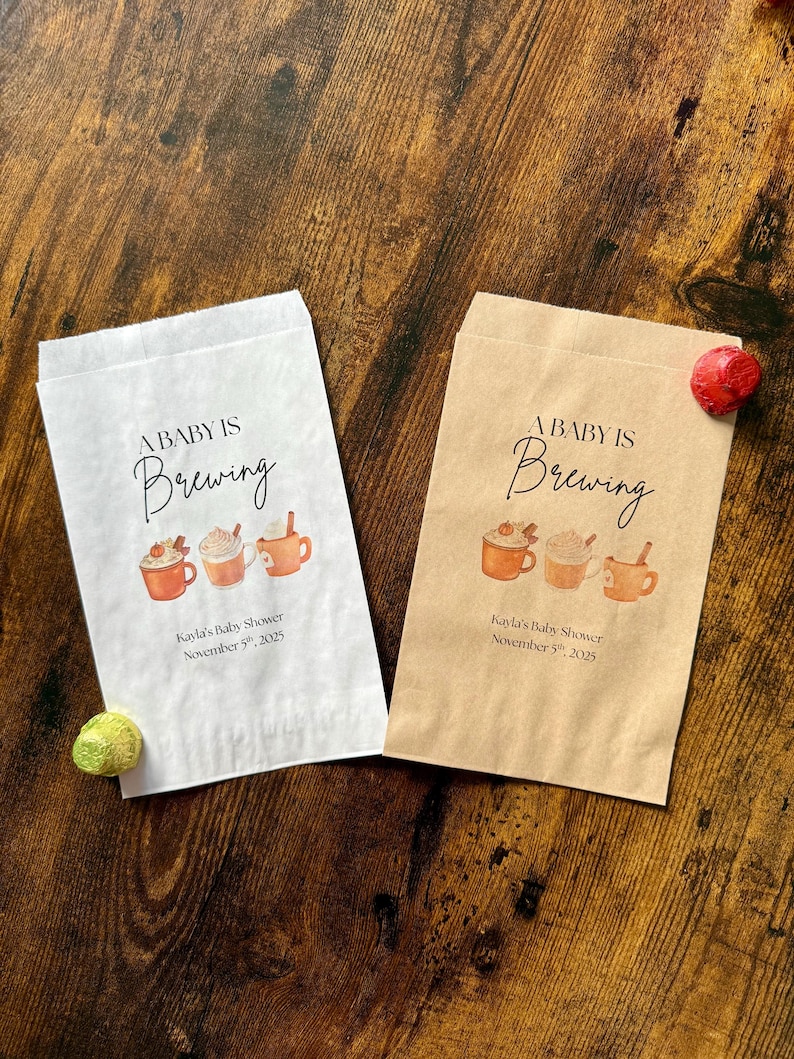 May include: Two paper treat bags, one white and one tan, with the text "A BABY IS Brewing" in elegant script. Below are illustrations of three mugs of coffee. The text "Kayla's Baby Shower November 5th, 2025" is printed below the mugs.
