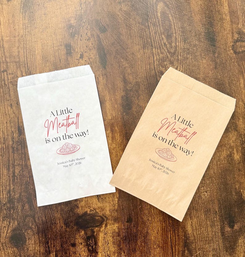 May include: Two paper favor bags, one white and one tan, with the text "A Little Meatball is on the way!" in burgundy script. A plate of spaghetti and meatballs is illustrated below the text. The bags are for Jessica's Baby Shower.