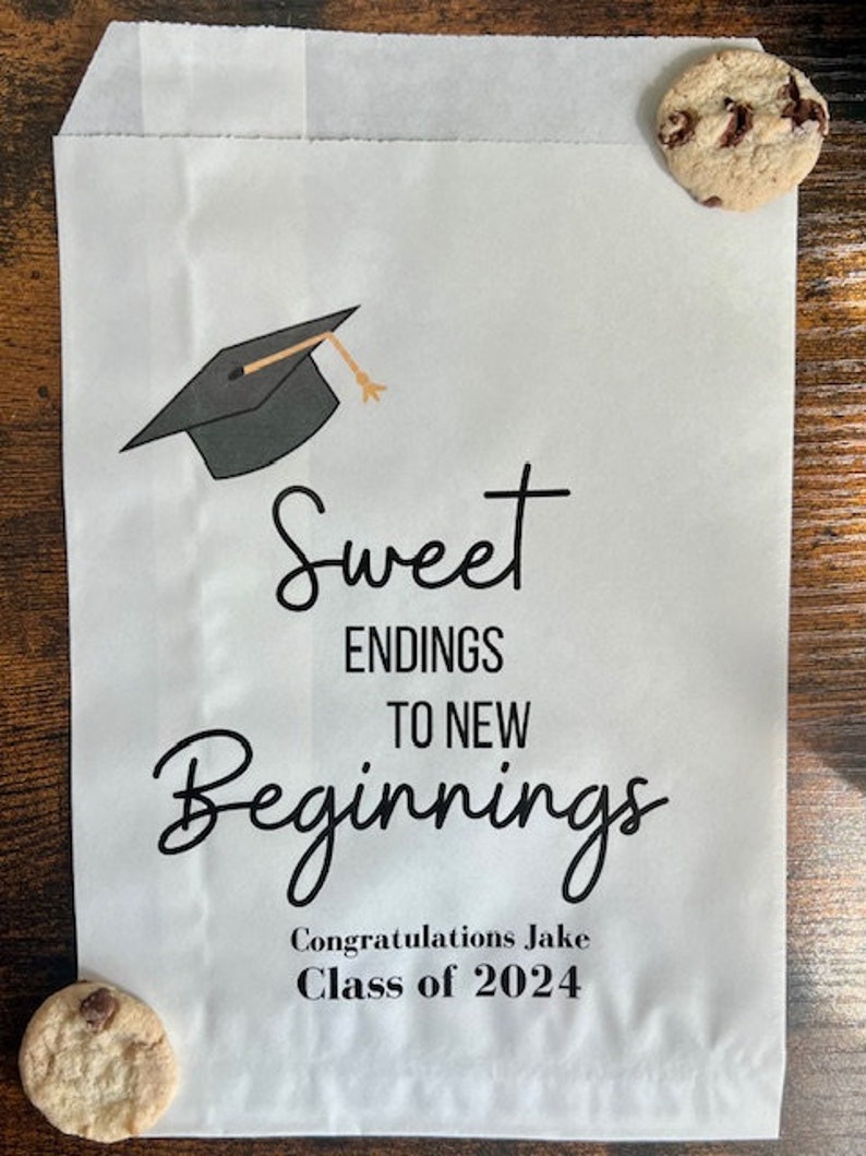 May include: White paper bag with a graduation cap graphic and the text "Sweet Endings to New Beginnings." The bag also includes the text "Congratulations Jake Class of 2024." Two chocolate chip cookies are placed on the bag.