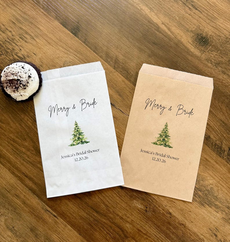 May include: Two rectangular paper favor bags, one white and one kraft brown, each printed with a green watercolor pine tree, the text Merry & Bride, and the personalized details Jessica's Bridal Shower 12.20.26, alongside a small chocolate treat.